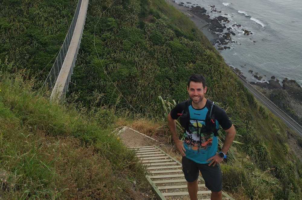 Estudiante en Nueva Zelanda chico moreno con ropa deportiva sonriendo a cámara y está en unas escaleras de una montaña